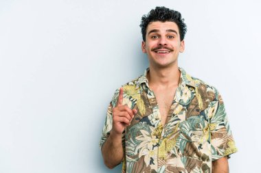 Mavi arka planda izole edilmiş genç beyaz adam bir numarayı parmağıyla gösteriyor..