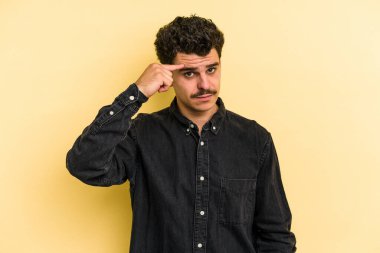 Sarı arka planda izole edilmiş genç beyaz bir adam şakağı parmağıyla işaret ediyor, düşünüyor ve bir göreve odaklanıyor..