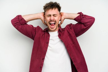 Beyaz arka planda izole edilmiş genç beyaz bir adam kulakları kulaklarıyla kapatıyor ve çok ses duymamaya çalışıyor..