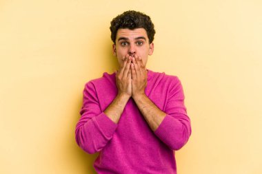 Sarı arka planda izole edilmiş genç beyaz adam elleriyle ağzını kapatırken şok oldu..