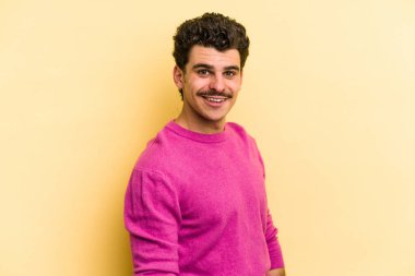 Sarı arka planda izole edilmiş genç beyaz adam ellerini kalçalarına koyuyor..