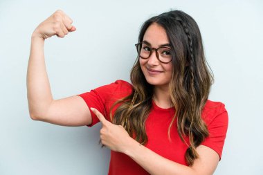 Mavi arka planda izole edilmiş genç beyaz kadın güçlü bir hareket sergiliyor kollarıyla, kadınsı gücün sembolü.