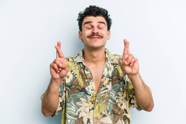 Kafkasyalı genç adam mavi arka planda izole edilmiş şans dilemek için şans diliyor.