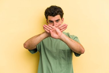 Sarı arka planda izole edilmiş genç beyaz adam inkar jesti yapıyor.