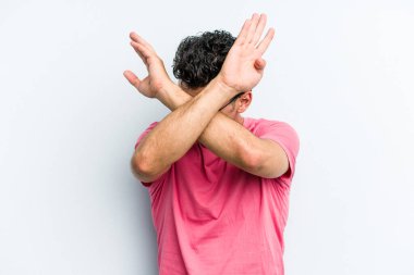 Kafkasyalı genç adam mavi arka planda izole edilmiş iki kolu çapraz tutuyor, inkar kavramı.