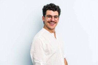 Kafkasyalı genç, mavi arka planda izole edilmiş. Kendine güvenen, kalçaları tutan biri..