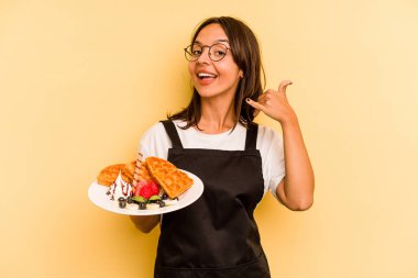 Sarı arka planda gözleme tutan Latin kökenli genç bir kadın cep telefonu hareketini parmaklarıyla gösteriyor..