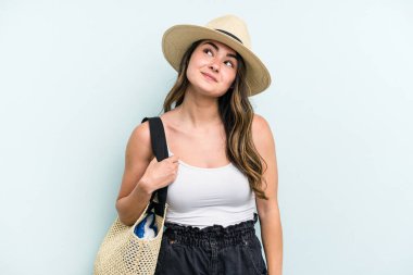 Young caucasian woman holding beach bag isolated on blue background dreaming of achieving goals and purposes