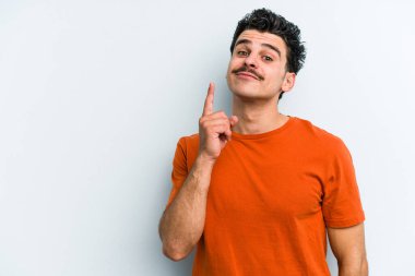 Mavi arka planda izole edilmiş genç beyaz adam bir numarayı parmağıyla gösteriyor..