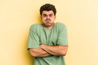 Sarı arka planda izole edilmiş genç beyaz adam yanakları patlatır, yorgun bir ifadeye sahiptir. Yüz ifadesi kavramı.