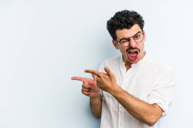 Mavi arka planda izole edilmiş genç beyaz adam işaret parmağıyla fotokopi alanını işaret ederek heyecan ve arzusunu ifade ediyor..
