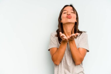 Mavi arka planda izole edilmiş genç İspanyol kadın gülümsüyor ve boş alanda bir şeyler gösteriyor..