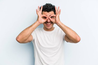 Mavi arka planda izole edilmiş genç beyaz adam gözlerinde sorun olmadığını gösteriyor.