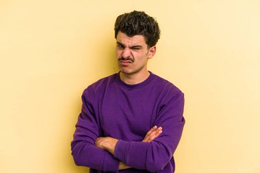 Sarı arka planda izole edilmiş genç beyaz adam alaycı bir ifadeyle kameraya bakıyor..