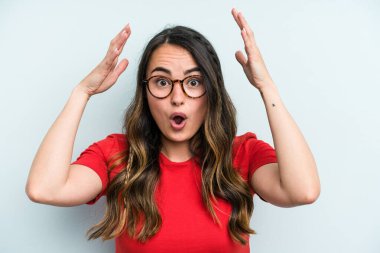 Mavi arka planda izole genç beyaz kadın zaferi ya da başarıyı kutluyor, şaşırıyor ve şok oluyor..