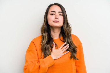 Beyaz arka planda izole edilmiş genç beyaz kadın yemin ediyor, elini göğsüne koyuyor..