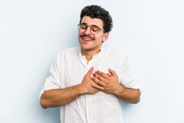 Mavi arka planda izole edilmiş beyaz bir genç, dost bir ifadeye sahip, avuçlarını göğsüne bastırıyor. Aşk konsepti.