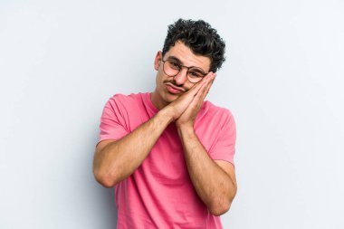 Mavi arka planda izole edilmiş genç beyaz adam esniyor. Ağzı eliyle kapatan yorgun bir hareket sergiliyor..