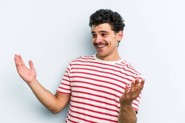 Kafkasyalı genç adam mavi arka planda izole edilmiş neşeli bir şekilde gülüyor. Mutluluk kavramı.