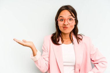 Mavi arka planda izole edilmiş genç İspanyol kadın mutlu bir şekilde gülüyor ve ellerini karnının üstünde tutarak eğleniyor..