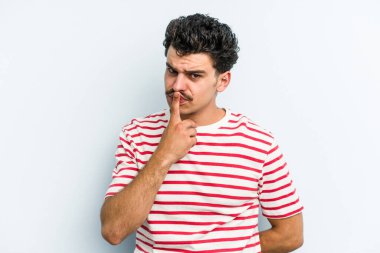 Kafkasyalı genç adam mavi arka planda izole edilmiş düşünüyor ve bakıyor, yansıtıyor, düşünüyor, bir fantezi kuruyor..