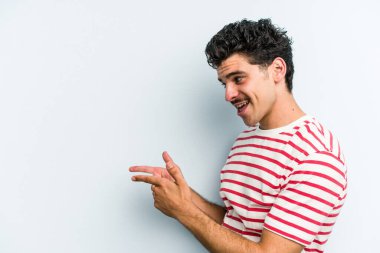 Kafkasyalı genç adam mavi arka plan noktalarında izole edilmiş başparmak uzakta, gülüyor ve kaygısız.