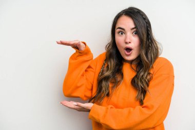 Beyaz arka planda izole genç beyaz kadın şok ve hayret içinde elleri arasında bir kopya alanı tutuyor.