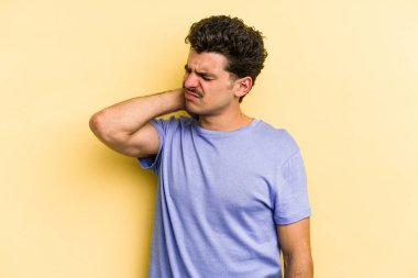 Sarı arka planda izole edilmiş genç beyaz bir adam stresten dolayı boynu ağrıyor, masaj yapıyor ve elle dokunuyor..