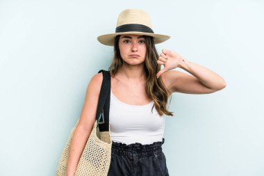 Young caucasian woman holding beach bag isolated on blue background showing a dislike gesture, thumbs down. Disagreement concept.
