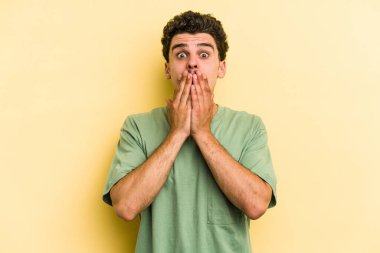 Sarı arka planda izole edilmiş genç beyaz adam elleriyle ağzını kapatırken şok oldu..