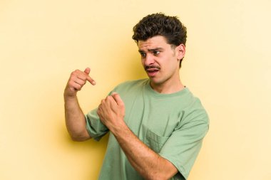 Sarı arka planda izole edilmiş genç beyaz adam parmağını göstererek şaşırdı ve gülümsedi..