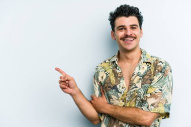 Mavi arka planda izole edilmiş genç beyaz adam işaret parmağıyla işaret ederek gülümsüyor..