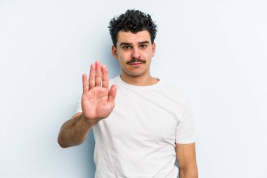 Mavi arka planda izole edilmiş genç beyaz adam gülümseyerek beş numarayı parmaklarıyla gösteriyor..