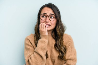 Mavi arka planda izole edilmiş, tırnak yiyen, gergin ve endişeli bir beyaz kadın..