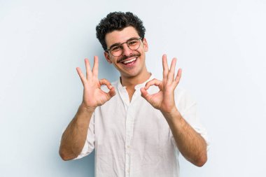 Kafkasyalı genç adam mavi arka planda izole edilmiş neşeli ve kendinden emin..