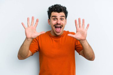 Mavi arka planda izole edilmiş genç beyaz adam hoş bir sürpriz alıyor, heyecanlı ve el kaldırıyor..