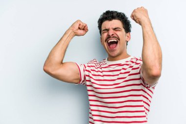 Mavi arka planda izole edilmiş genç beyaz bir adam zaferden sonra yumruğunu kaldırıyor, kazanan konsept..