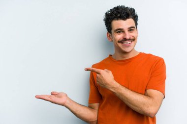 Kafkasyalı genç adam mavi arka planda izole edilmiş. Elinde palmiye ağacının bir kopyası olduğu için heyecanlı..