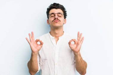 Mavi arka planda izole edilmiş genç beyaz adam yorucu bir günün ardından rahatlıyor. Yoga yapıyor..