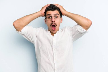 Kafkasyalı genç adam mavi arka planda izole edildi. Şaşırdı ve şok oldu..