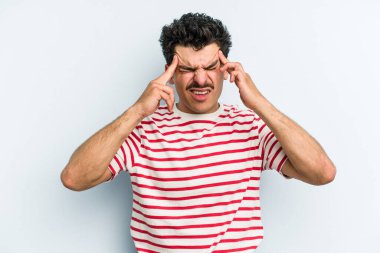 Genç beyaz adam mavi arka planda izole edilmiş tapınaklara dokunuyor ve başı ağrıyor..