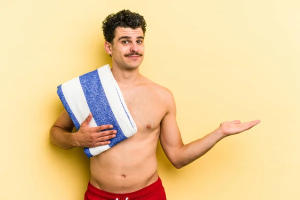 Young Caucasian Man Holding Beach Towel Isolated Yellow Background Showing — 图库照片