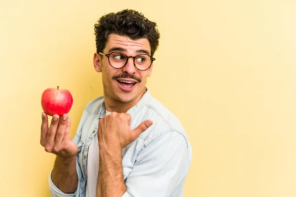 Young Caucasian Man Holding Apple Isolated Yellow Background Points Thumb — Stock Fotó