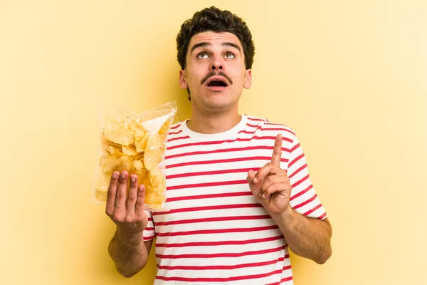 Young Caucasian Man Holding Bag Chips Isolated Yellow Background Pointing — Stockfoto