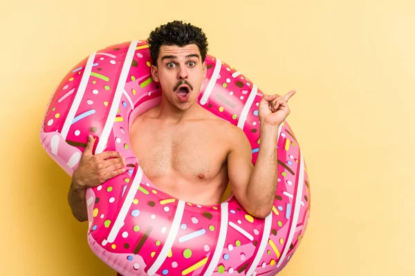 Young Caucasian Man Holding Inflatable Donut Isolated Yellow Background Pointing — Stock fotografie