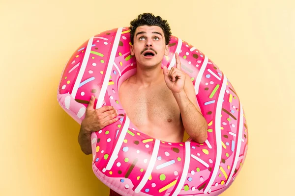 Young Caucasian Man Holding Inflatable Donut Isolated Yellow Background Pointing — 图库照片