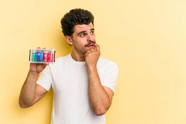 Young Caucasian Man Holding Batteries Isolated Yellow Background Relaxed Thinking — Fotografia de Stock