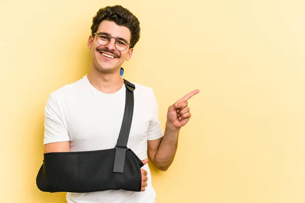 Young Caucasian Man Broke Hand Isolated Yellow Background Smiling Pointing — Stock Fotó