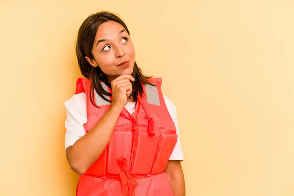 Ung Latinamerikansk Kvinna Håller Flytväst Isolerad Gul Bakgrund Tittar Sidled — Stockfoto