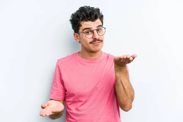 Young Caucasian Man Isolated Blue Background Makes Scale Arms Feels — Stock Photo, Image